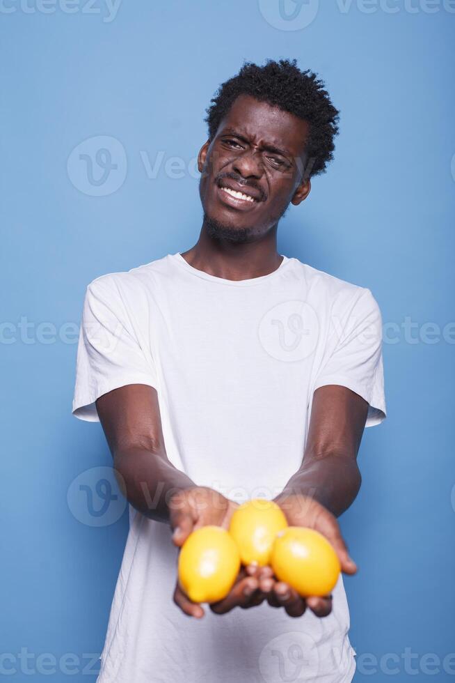 afrikanisch amerikanisch Person halten Zitronen zum gesund Vegetarier Diät. Mann präsentieren Gelb Zitrusfrüchte Früchte im Hände zum natürlich Ernährung mit Vitamine. Erwachsene zeigen frisch saftig Früchte zu Kamera. foto