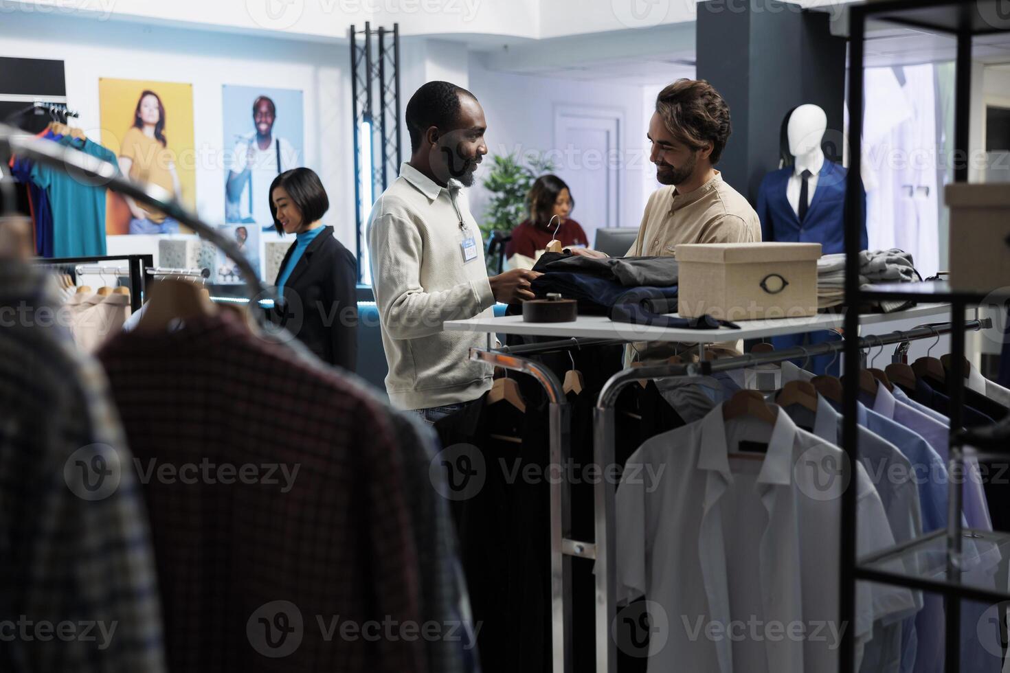 lächelnd Assistent halten Aufhänger mit stilvoll Jacke, präsentieren Mode Trend zu Kunde im Kleidung speichern. Boutique Mitarbeiter reden mit Klient und Portion zu machen bekleidung Wahl foto