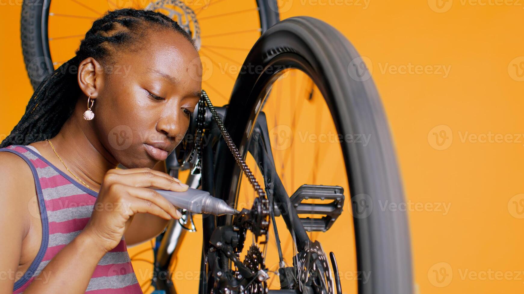 bipoc Techniker mit spezialisiert kleben zu Reparatur gebrochen Fahrrad Kette, Orange Studio Hintergrund. Fachmann bewirbt sich Klebstoff auf Fahrrad Komponenten während Instandhaltung Verfahren, schließen oben Schuss, Kamera b foto