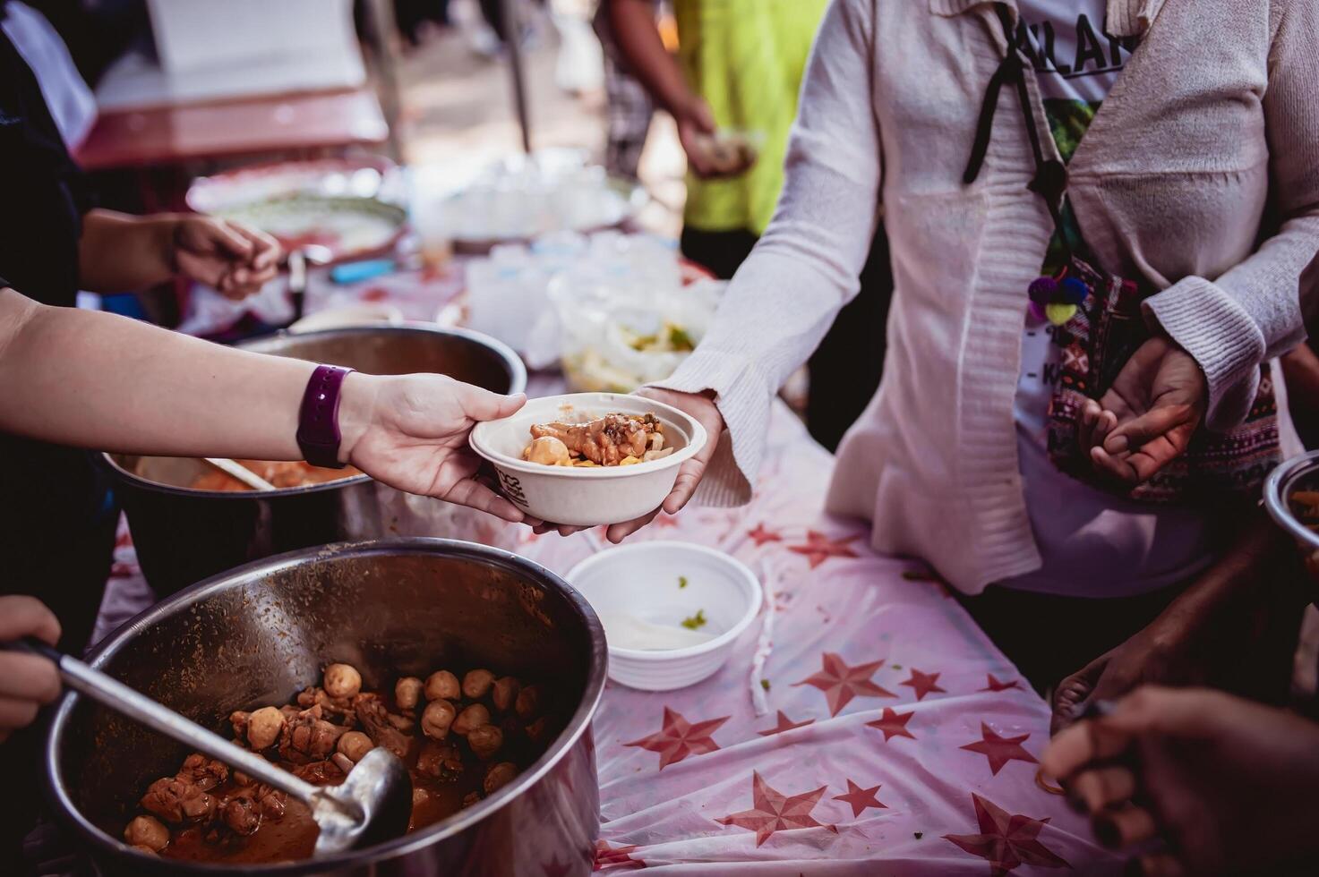 das Hand von das Wanderer erweitert zu erhalten Essen von Spenden. mit Freiwillige schöpfen Essen foto