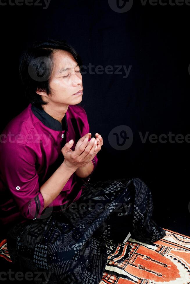 Seite Aussicht von ein Mann beten auf ein Gebet Matte auf ein schwarz Hintergrund. foto