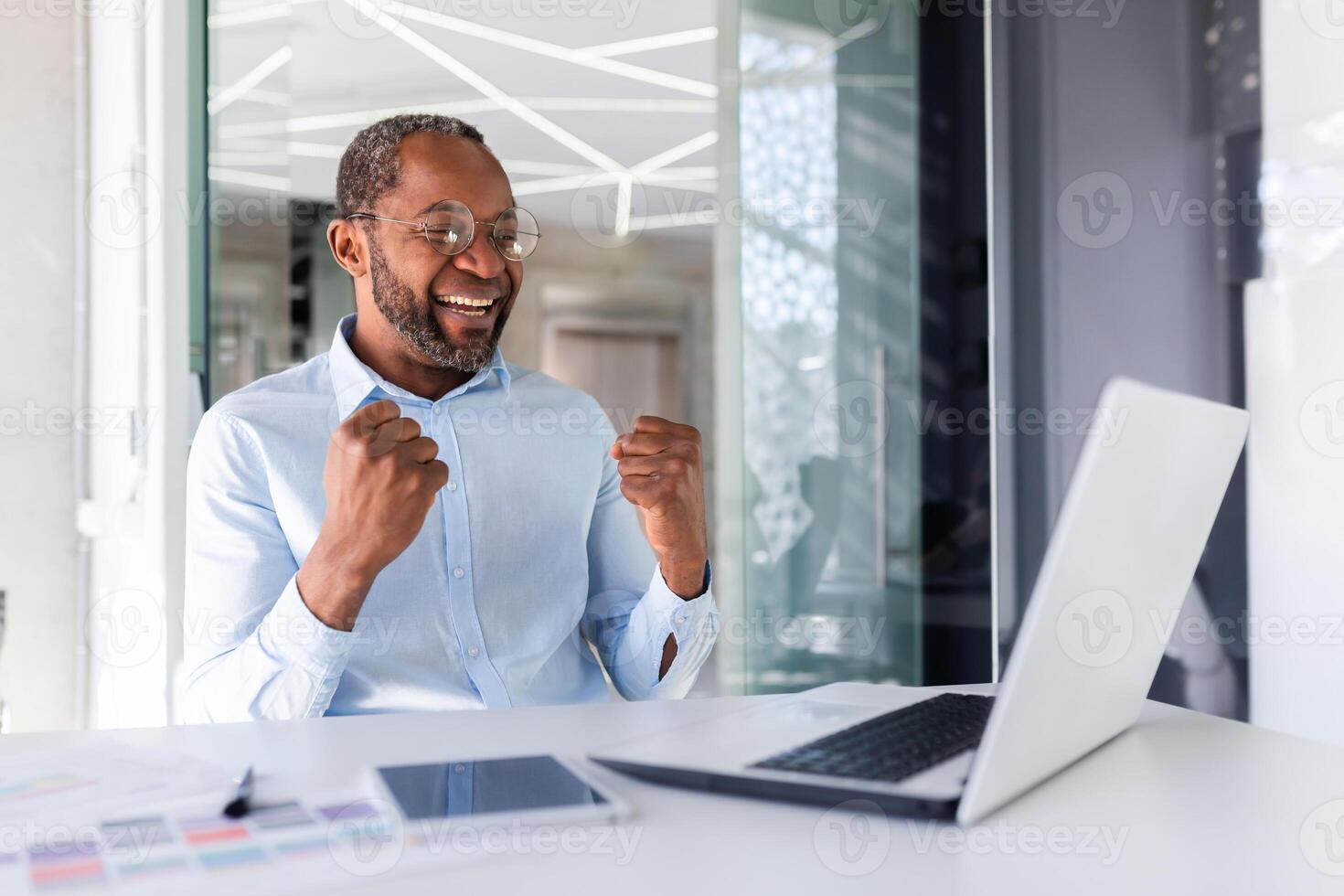 erfolgreich Mann Arbeiten Innerhalb Büro, Mann halten Hände oben Geste von Sieg und Erfolg, afrikanisch amerikanisch reifen Boss feiern Sieg und Erfolg, Geschäftsmann empfangen online Benachrichtigung mit Sieg. foto