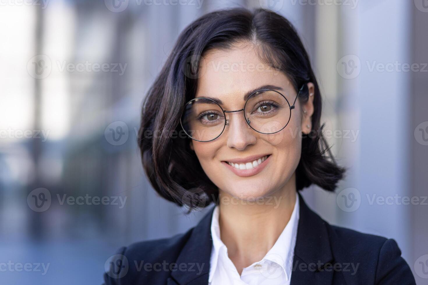 Nahansicht Foto von ein jung schön erfolgreich weiblich Anwalt im ein passen und Brille lächelnd beim das Kamera und Stehen außen.