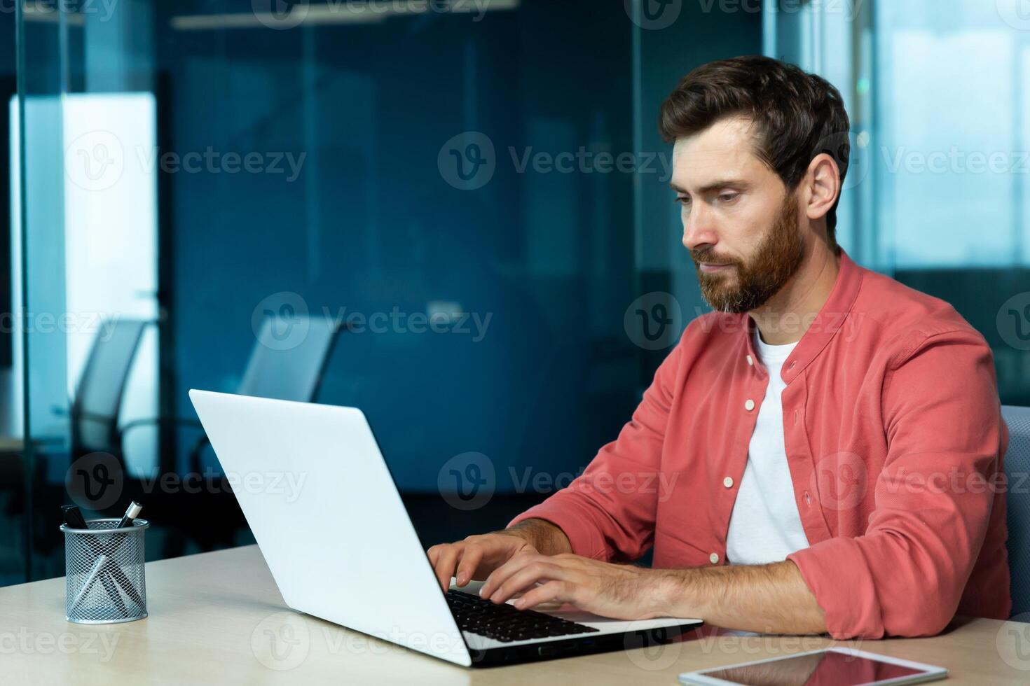 ernst konzentriert Denken Geschäftsmann Arbeiten mit Laptop Innerhalb Büro beim Arbeitsplatz, Mann Tippen auf Klaviatur, vorbereiten online Präsentation und finanziell Buchhaltung Bericht. foto