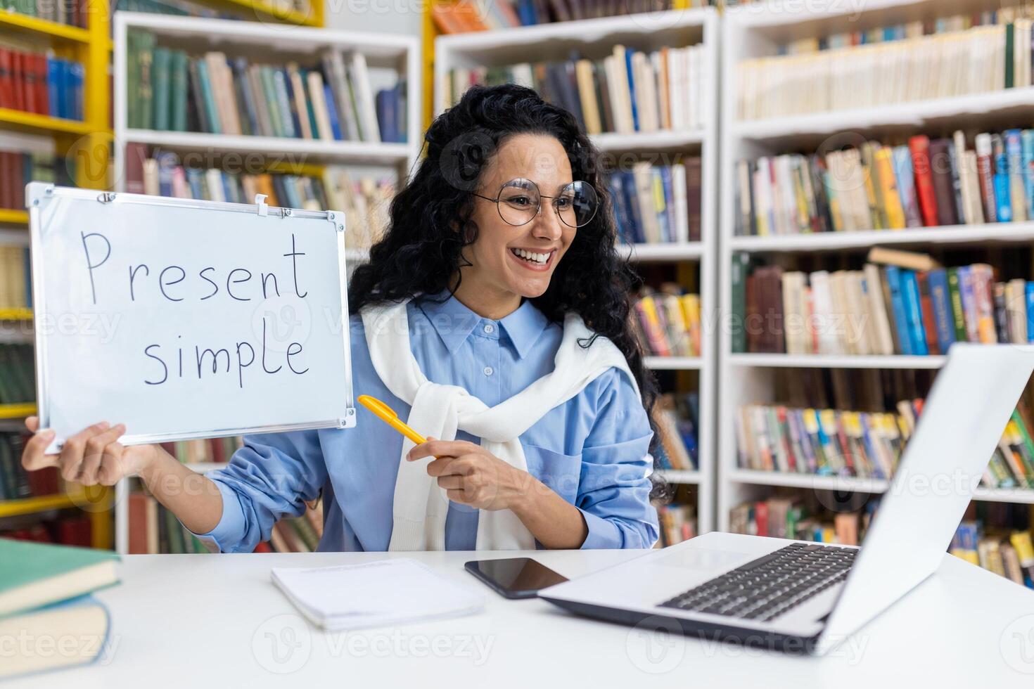 begeistert online Englisch Lehrer halten ein Tafel, erklären Grammatik im ein virtuell Klasse inmitten ein Bücherregal Hintergrund. foto