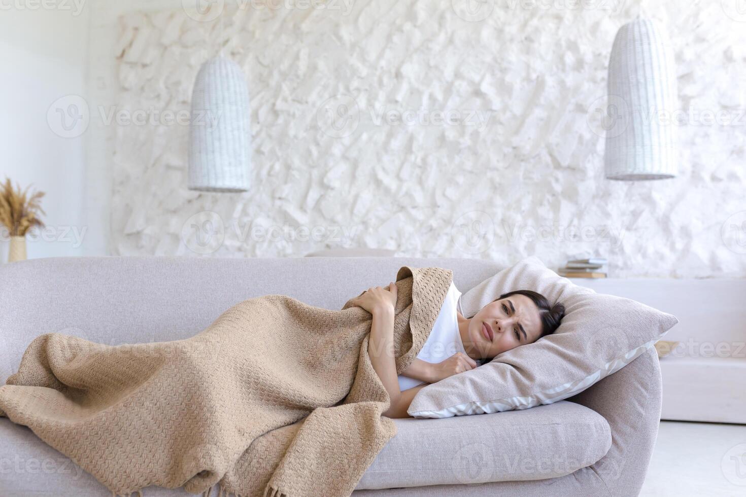 ein müde Frau ist Lügen beim Zuhause auf das Sofa bedeckt mit ein Decke. krank, Gefühl schlecht, Depression foto
