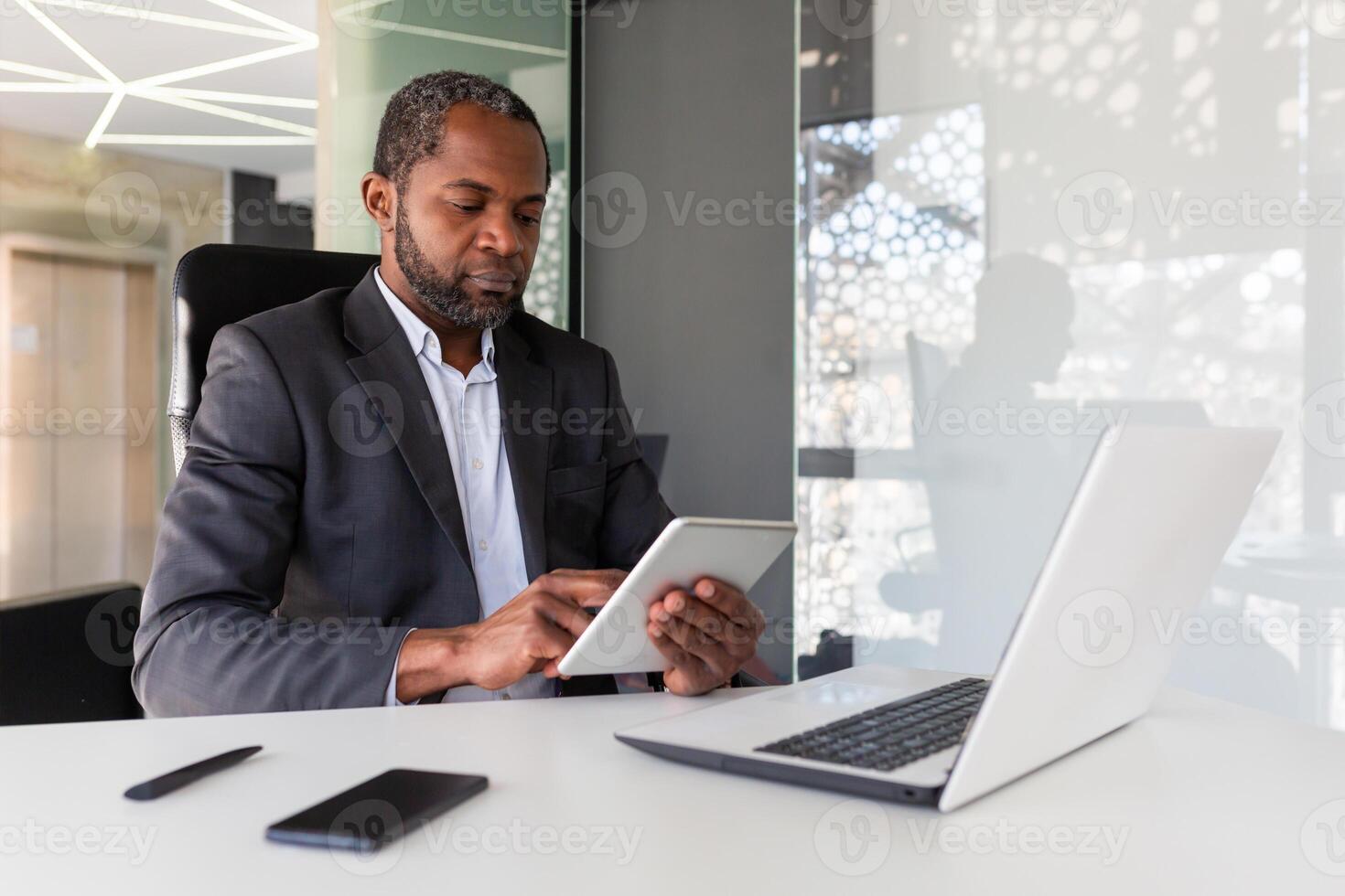 ernst Denken Geschäftsmann Arbeiten Innerhalb Büro, mit Tablette Computer, afrikanisch amerikanisch reifen und zuversichtlich Boss mit App beim Arbeitsplatz, lesen finanziell Performance Indikatoren. foto