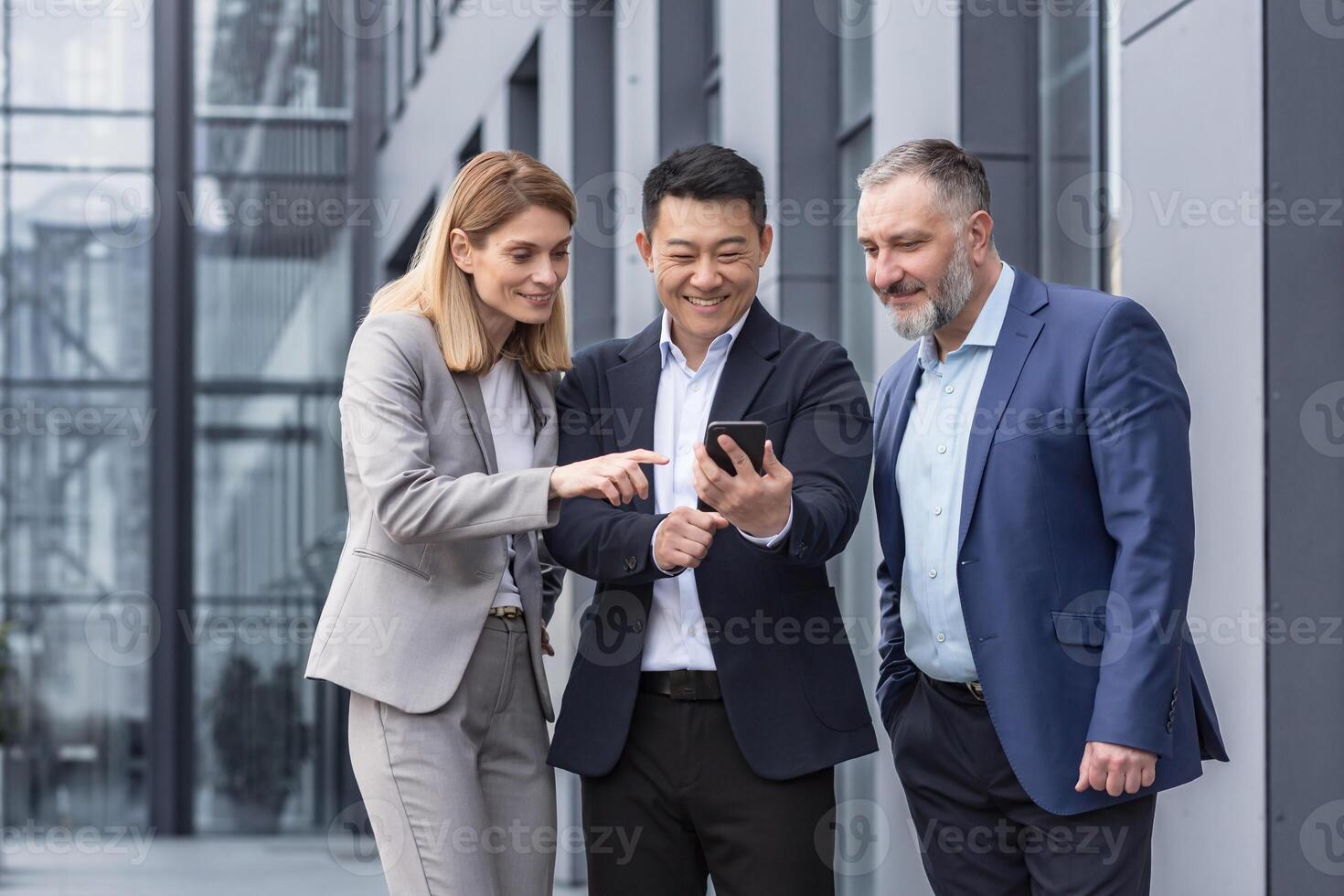 vielfältig Geschäft Gruppe, drei männlich und weiblich Arbeitskräfte draußen Büro Gebäude fröhlich lächelnd und glücklich Aufpassen auf Telefon foto