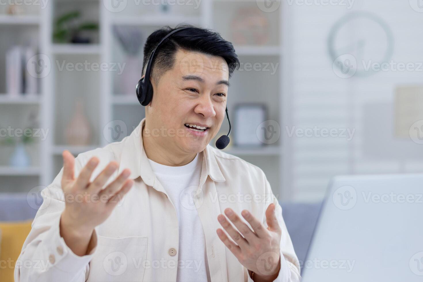 ein heiter asiatisch Mann engagiert im ein lebhaft Konversation mit ein Headset im ein hell, ordentlich organisiert Zuhause Büro Einstellung, demonstrieren Fernbedienung Arbeit Kommunikation. foto