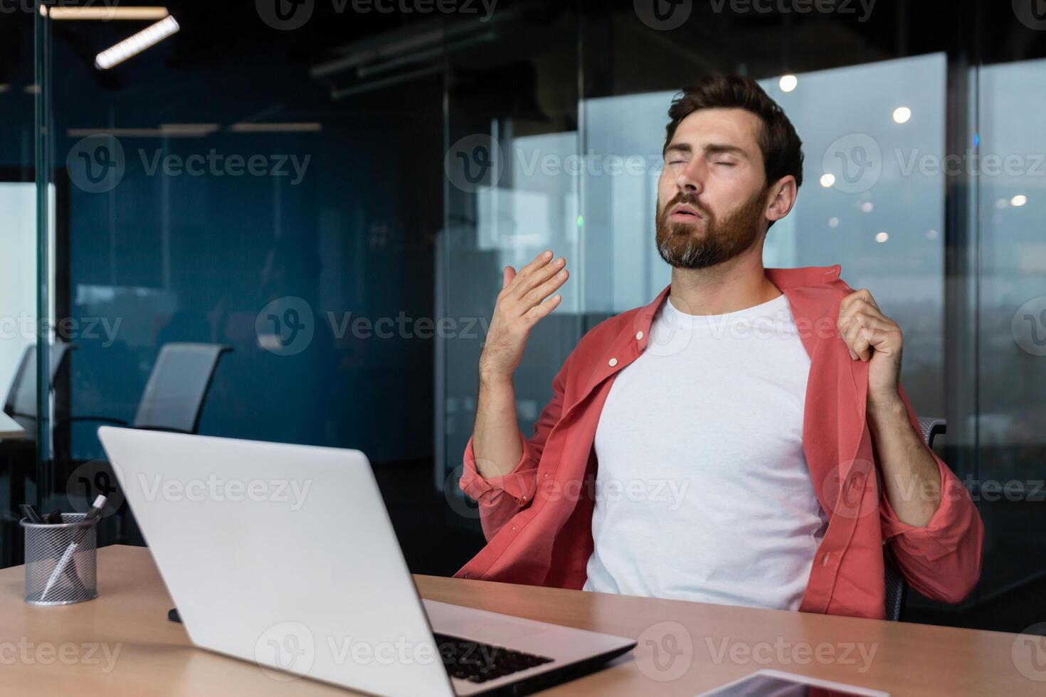 es ist heiß im das Büro, ein Geschäftsmann im ein rot Hemd ist heiß, das Luft Conditioner ist nicht Arbeiten, versuchen zu cool runter, ein Mann Innerhalb das Büro ist Arbeiten mit ein Laptop. foto