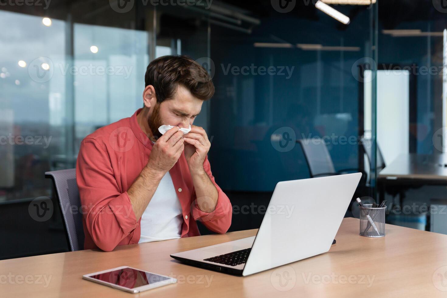 krank Mann beim Arbeit hat Grippe und kalt, Geschäftsmann Niesen und Husten beim Arbeitsplatz Arbeiten Innerhalb Büro beim Schreibtisch mit Laptop beim arbeiten. foto