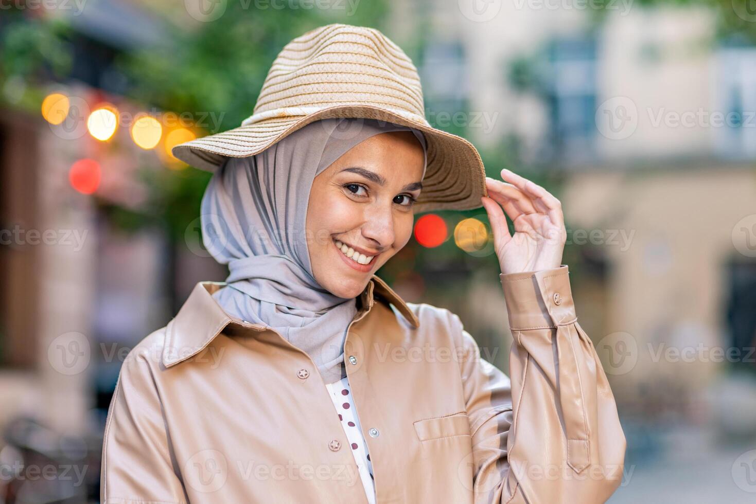 Porträt von attraktiv Muslim Frau tragen Hijab und berühren Stroh Hut mit spielerisch Gesichts- Ausdruck. Erfreut Dame kombinieren Kopfbedeckungen und Gefühl bereit zum Ferien Jahreszeit im stilvoll Outfit. foto