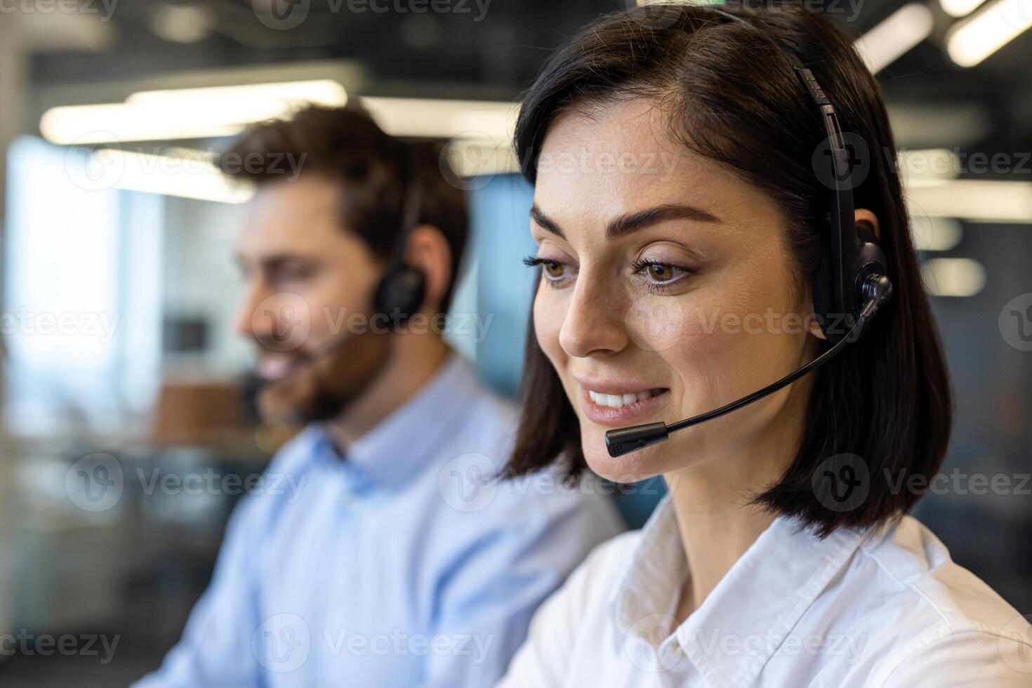 Porträt von lächelnd jung Frau im kabellos Headset und Weiß Hemd suchen voraus mit Lächeln Nächster zu männlich Mitarbeiter. Anruf Center Angestellte beginnend Neu Tag und bereit zum Bereitstellung Beratung Dienstleistungen. foto