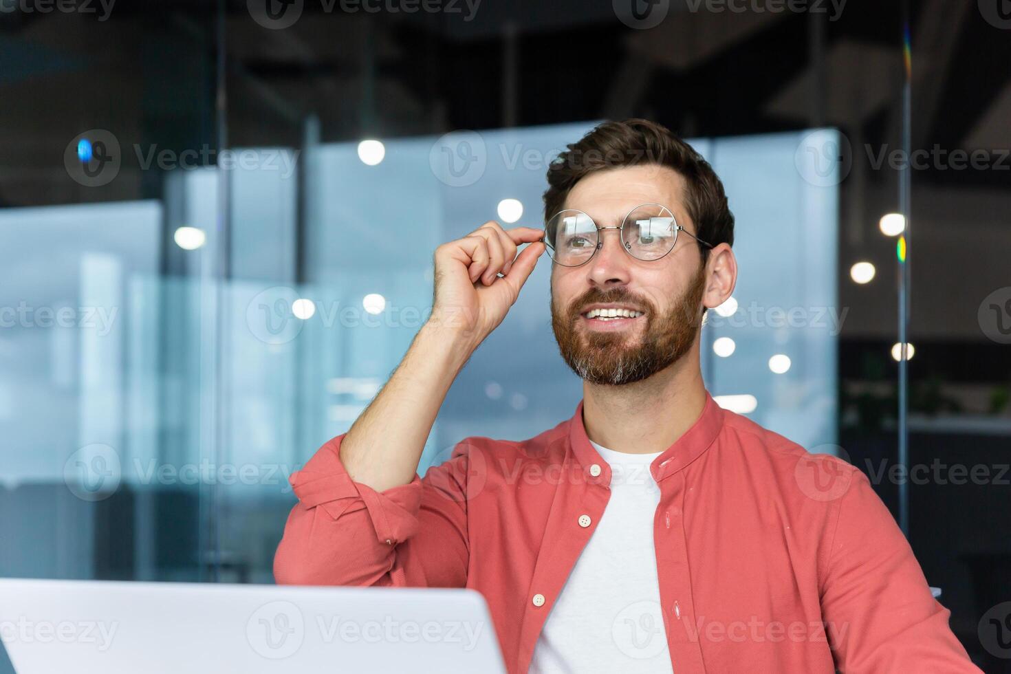 lächelnd verträumt Geschäftsmann Innerhalb Büro beim Arbeitsplatz, erfahren und erfolgreich Programmierer Ingenieur lächelnd und suchen aus Fenster, zufrieden mit Ergebnisse von Leistung beim arbeiten. foto