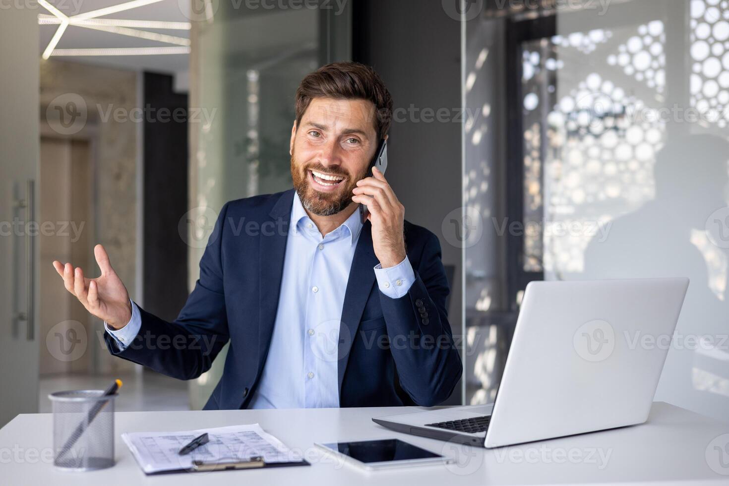 Porträt von ein erfolgreich und lächelnd jung Mann Geschäftsmann, Verkäufer, Makler emotional reden auf das Telefon mit Kunden, Sitzung beim das Schreibtisch im das Büro und suchen beim das Kamera. foto