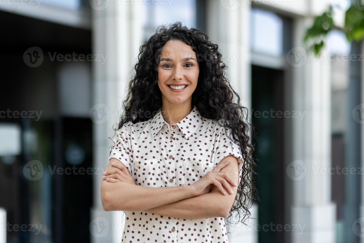 lächelnd Fachmann Frau mit lockig Haar auf ein brechen draußen in der Nähe von korporativ Büro, vorbildlich Geschäft Vertrauen. foto