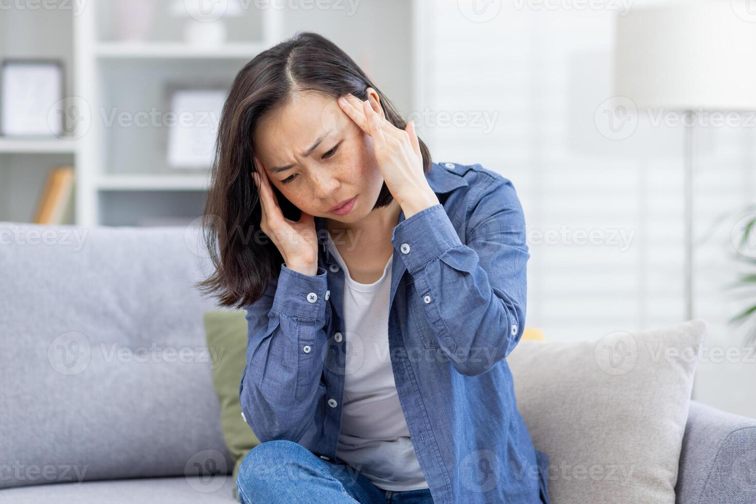 krank Frau allein beim heim, asiatisch deprimiert Frau haben stark Kopfschmerzen, Sitzung auf Sofa im Leben Zimmer beim heim, halten Hände zu Kopf von Schmerz. foto