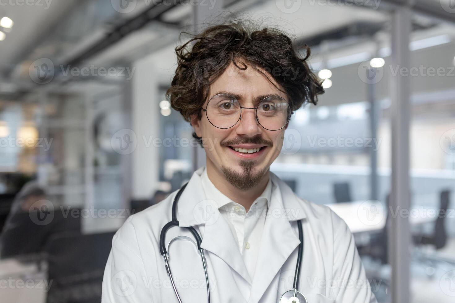 ein Arzt im ein Weiß medizinisch Mantel steht im seine Büro, halten ein Stethoskop. Mann schließen oben Nachsehen in Kamera Lächeln foto