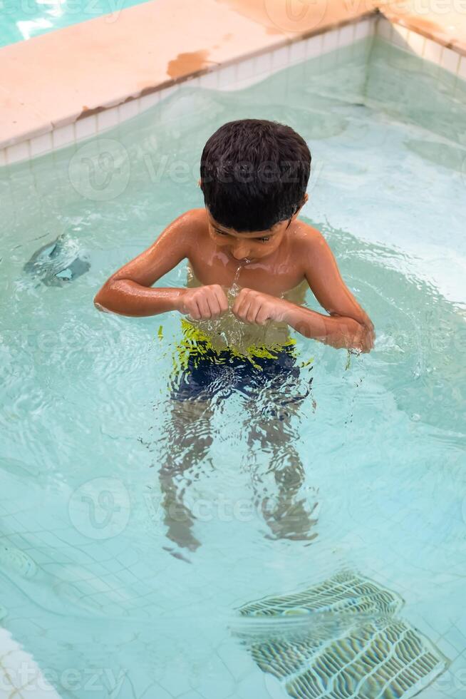 glücklich indisch Junge Schwimmen im ein Schwimmbad, Kind tragen Schwimmen Kostüm entlang mit Luft Tube während heiß Sommer- Urlaube, Kinder Junge im groß Schwimmen Schwimmbad. foto