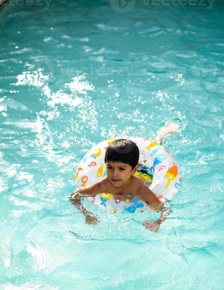 glücklich indisch Junge Schwimmen im ein Schwimmbad, Kind tragen Schwimmen Kostüm entlang mit Luft Tube während heiß Sommer- Urlaube, Kinder Junge im groß Schwimmen Schwimmbad. foto