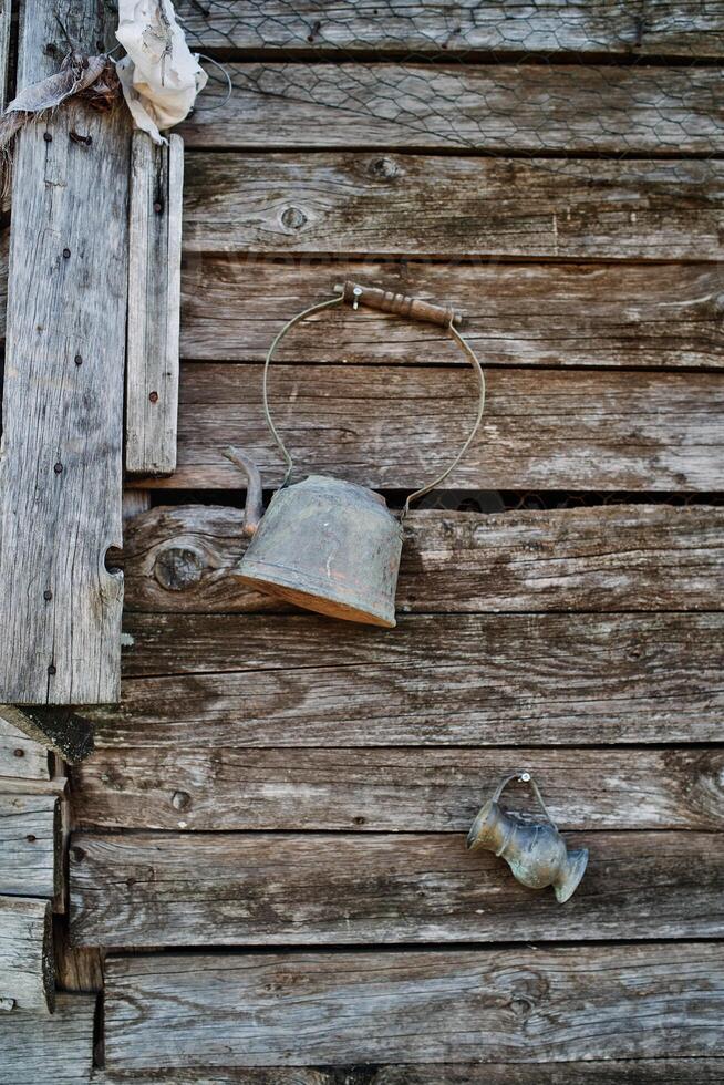 Antiquität Teekanne mit ein groß Griff und ein klein Krug hängen auf ein alt unbemalt hölzern Mauer foto