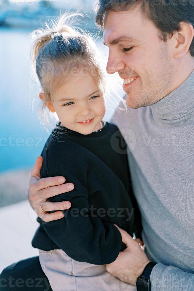 lächelnd Papa suchen beim wenig Mädchen Sitzung auf seine Runde während umarmen ihr foto