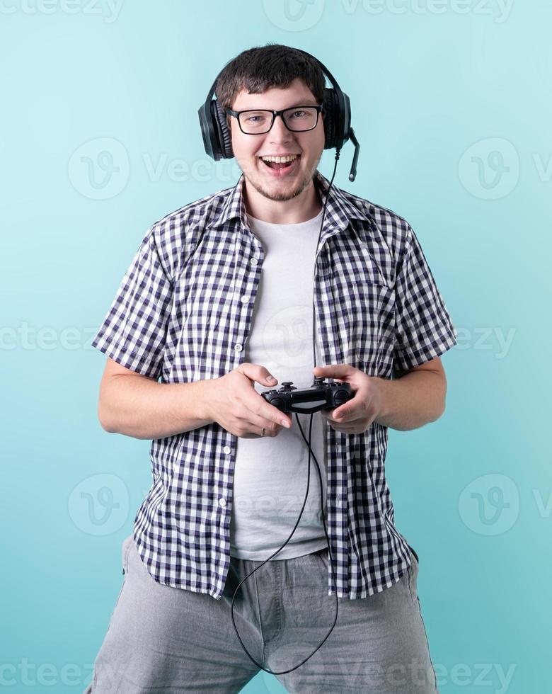 Glücklicher lachender junger Mann, der Videospiele spielt, die einen Joystick auf blauem Hintergrund halten foto