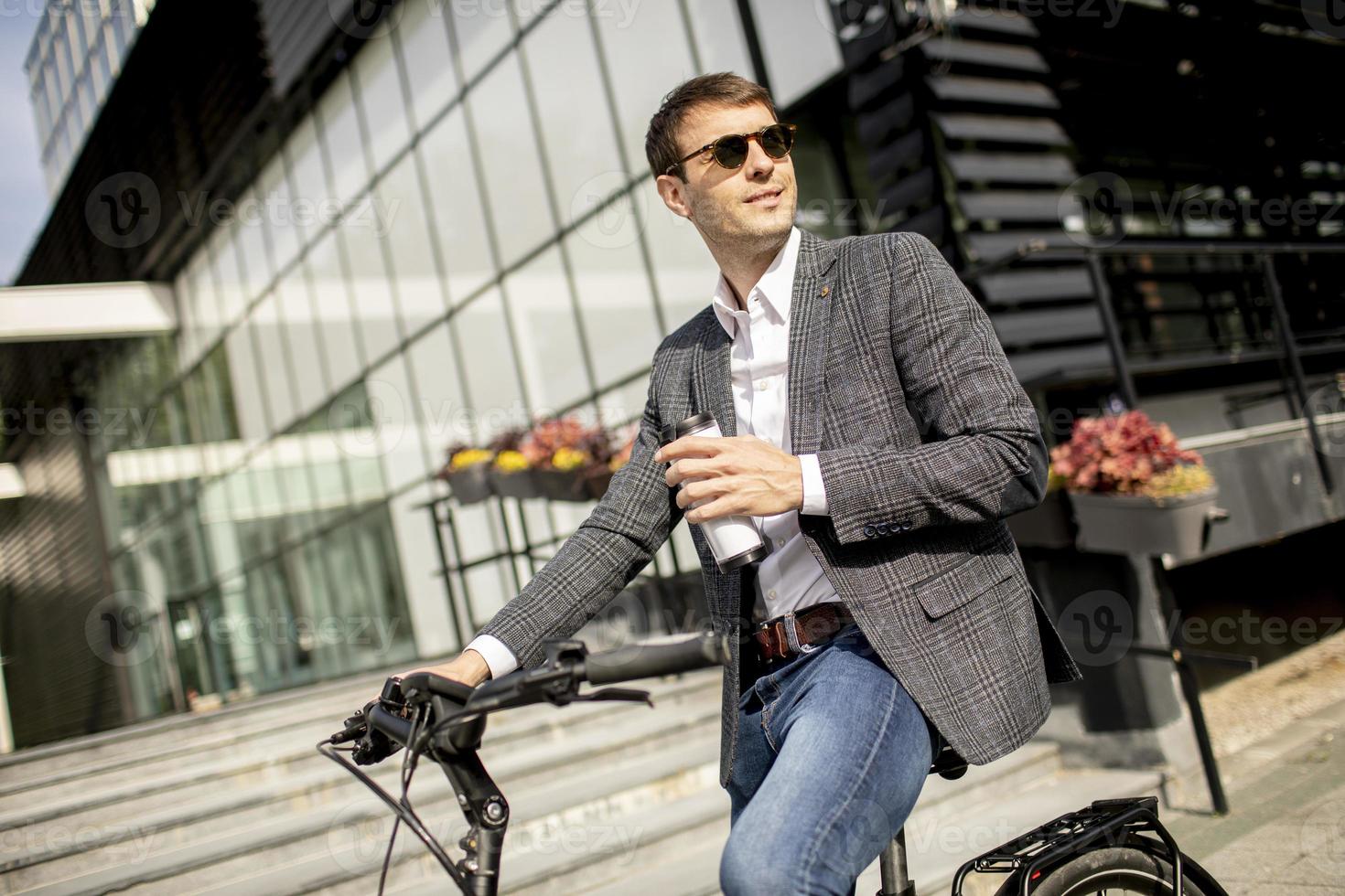junger Geschäftsmann auf dem E-Bike mit Kaffeetasse zum Mitnehmen foto