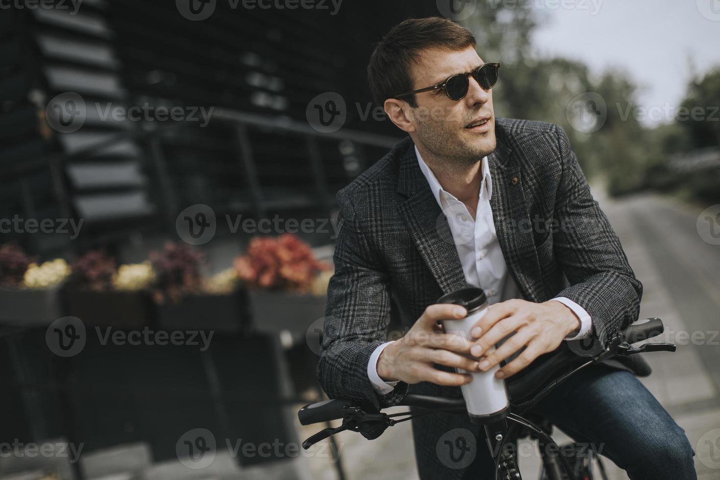 junger Geschäftsmann auf dem E-Bike mit Kaffeetasse zum Mitnehmen foto