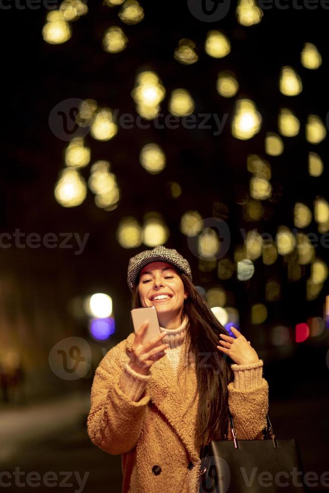 hübsche junge frau, die ihr handy zur weihnachtszeit auf der straße benutzt foto