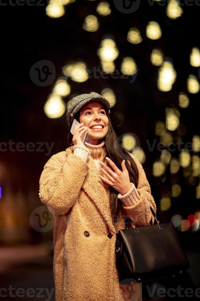 hübsche junge frau, die ihr handy zur weihnachtszeit auf der straße benutzt foto