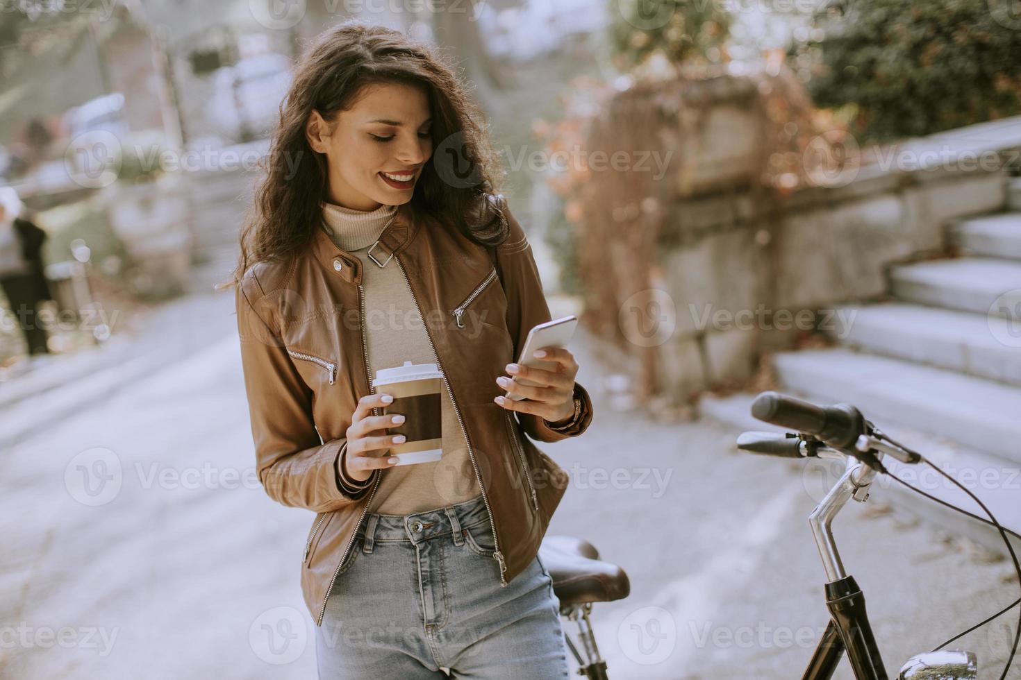 junge Frau mit Handy trinkt Kaffee, um am Herbsttag mit dem Fahrrad zu fahren foto