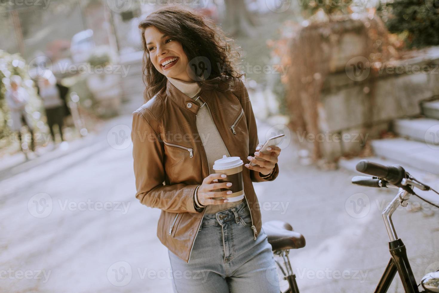 junge Frau mit Handy trinkt Kaffee, um am Herbsttag mit dem Fahrrad zu fahren foto