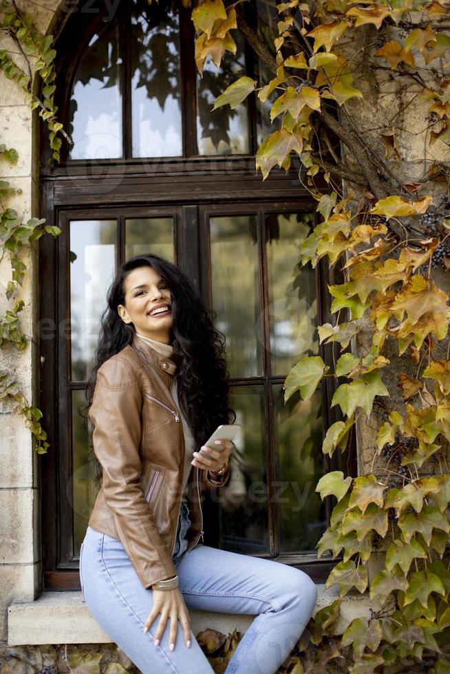 junge Frau mit Handy beim Sitzen auf der Fensterdichtung im Herbst foto