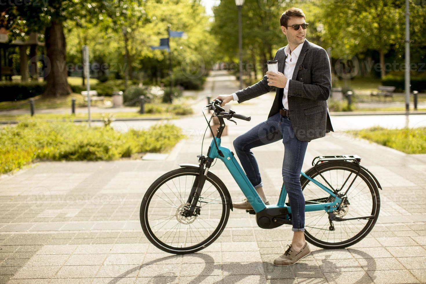 junger Geschäftsmann auf dem E-Bike mit Kaffeetasse zum Mitnehmen foto