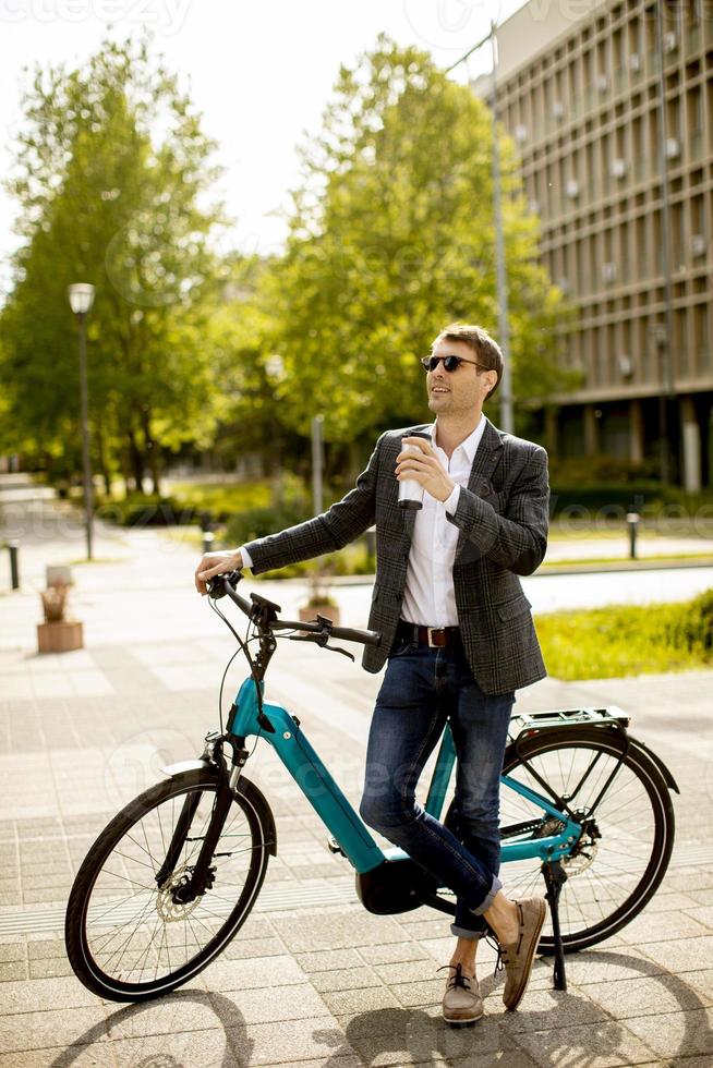 junger Geschäftsmann auf dem E-Bike mit Kaffeetasse zum Mitnehmen foto