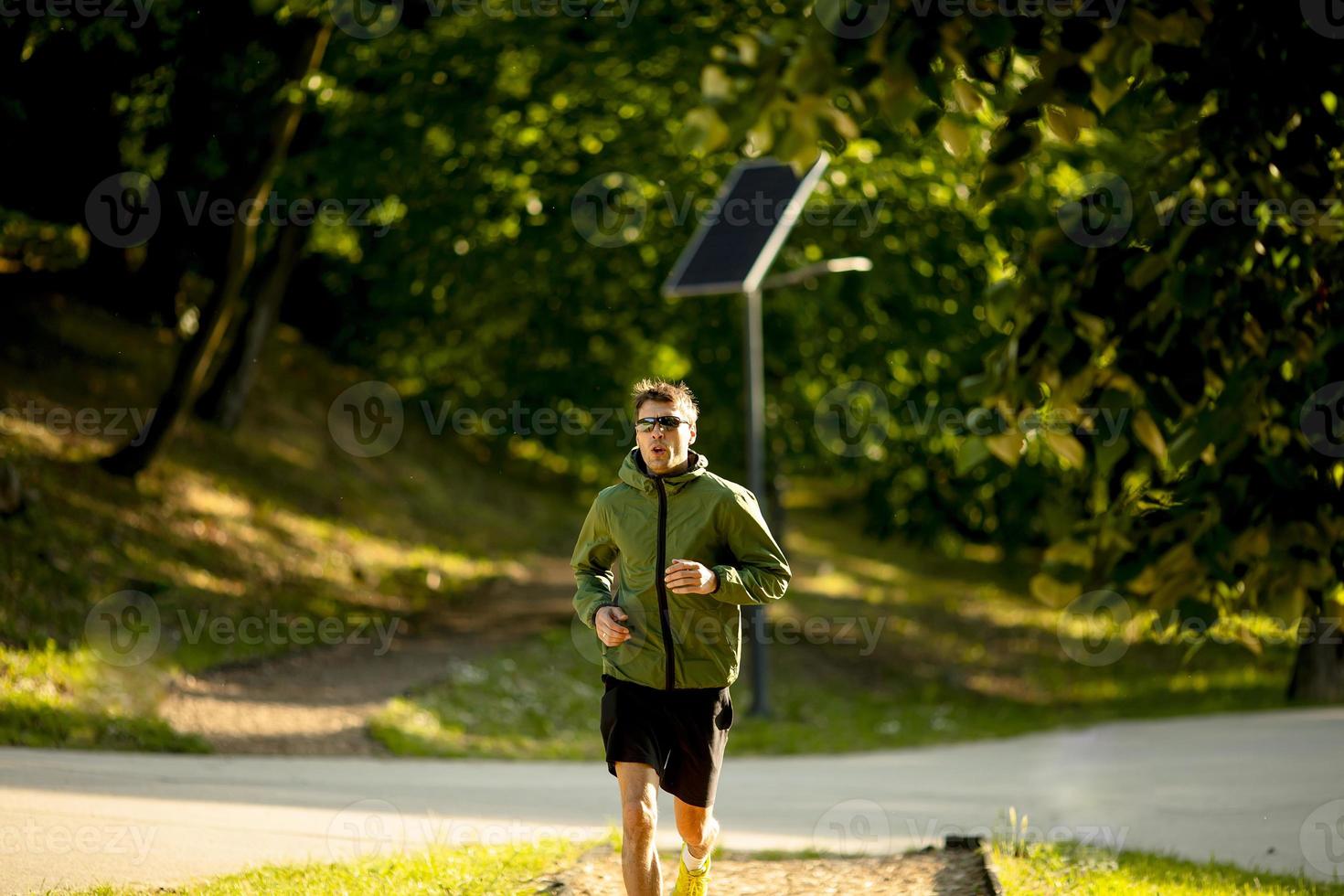 athletischer junger Mann, der beim Training im sonnigen grünen Park läuft foto