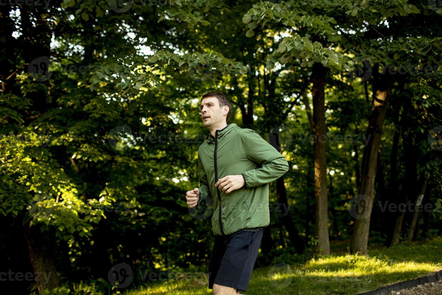 athletischer junger Mann, der beim Training im sonnigen grünen Park läuft foto