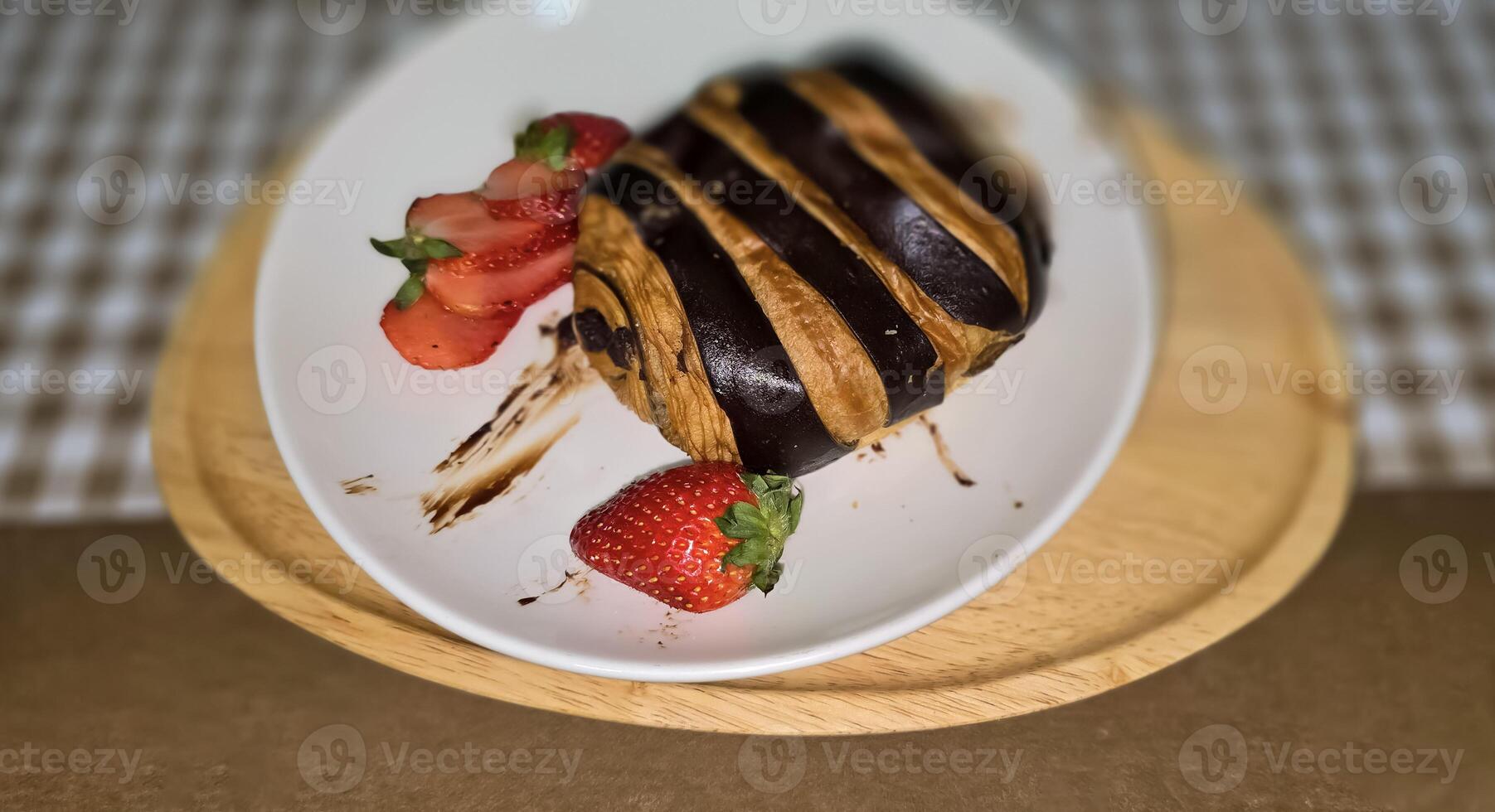 frisch hausgemacht gestreift Schokolade Croissant mit Schokolade Füllung auf ein runden Weiß Platte, serviert mit frisch Erdbeere foto