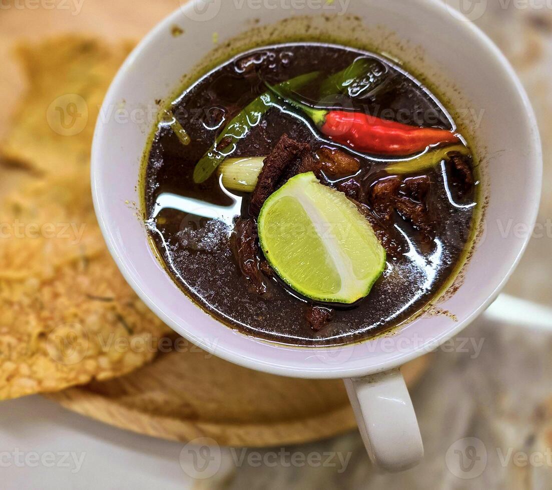 Rohon oder indonesisch schwarz Rindfleisch Suppe, schwarz Farbe sind von indonesisch Nuss namens Kluewek. serviert mit Kalk, Chili Paste, gesalzen Ei, und tempe Cracker. perfekt zum Rezept, Artikel, oder irgendein Kochen foto