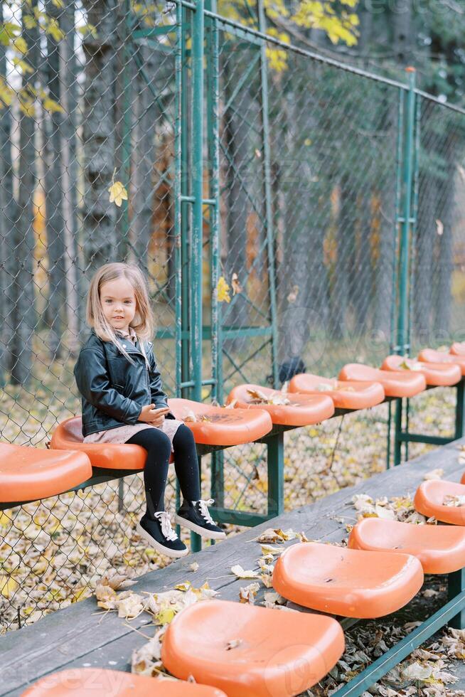 wenig Mädchen sitzt auf ein Sitz auf ein Spielplatz umgeben durch ein Gittergewebe Zaun foto