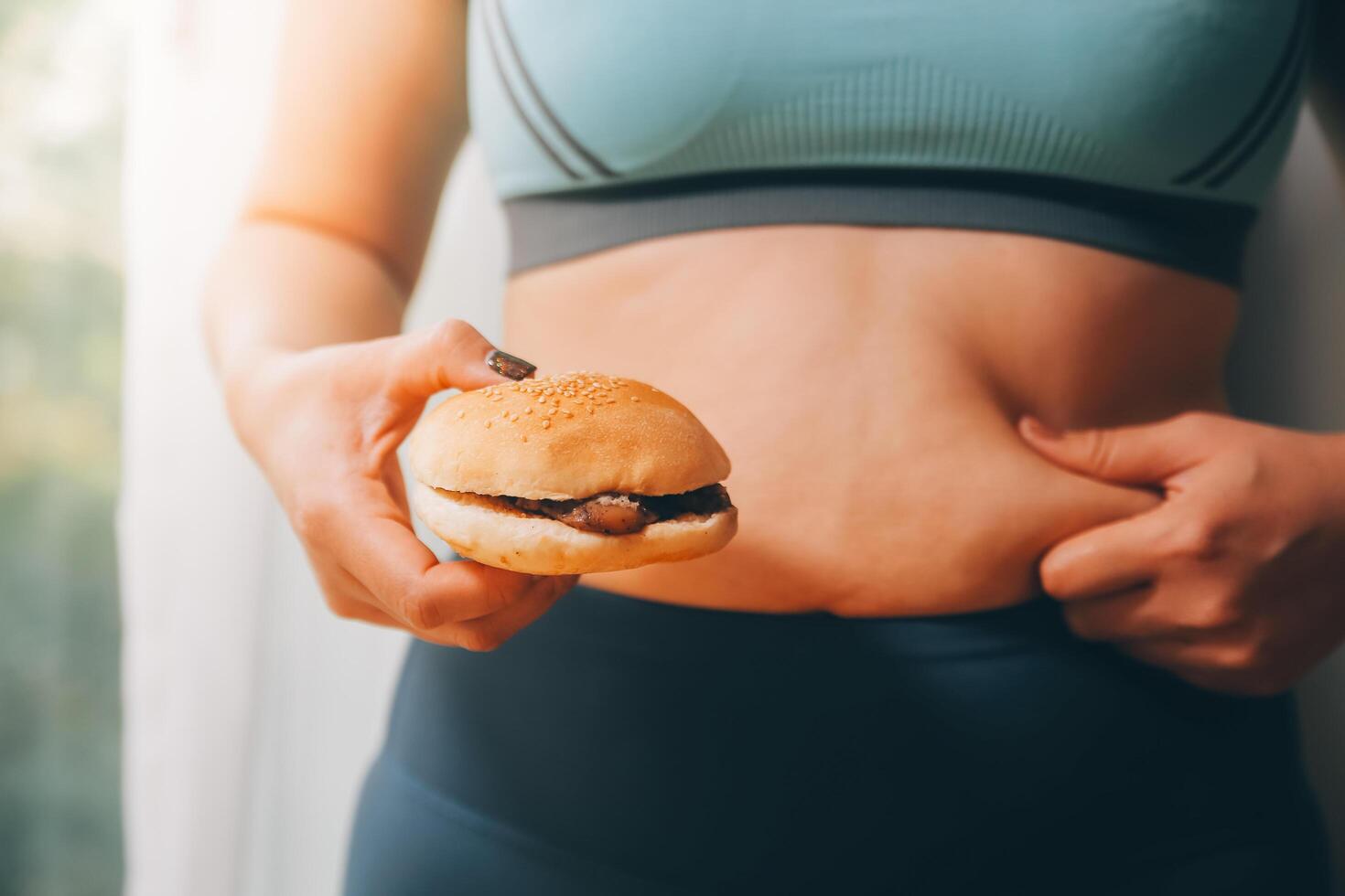 Porträt von fettleibig Frau sieht aus traurig während Kneifen ihr Bauch Fett umgeben durch Müll Lebensmittel. Diät Scheitern Konzept foto