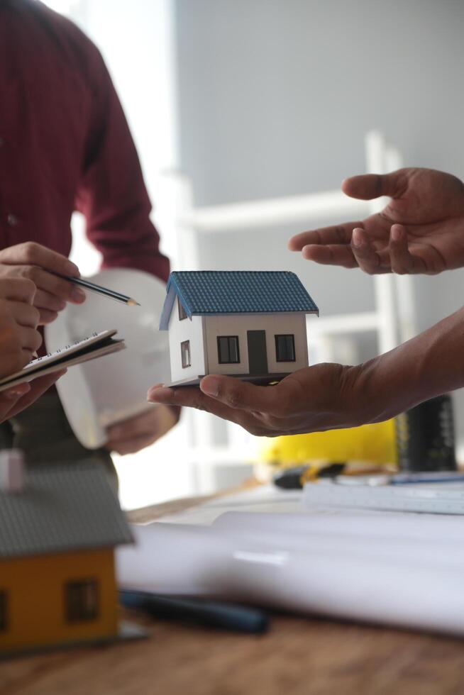 Ingenieure sind Beratung das Mannschaft zu Design ein architektonisch Struktur zum Kunden mit Blaupausen und Gebäude Modelle zu Arbeit beim Büro. foto