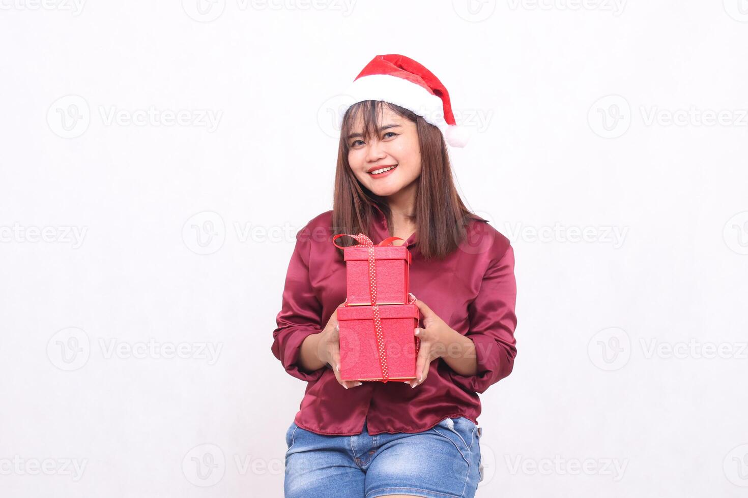 schön jung asiatisch indonesisch Mädchen lächelnd bringen Geschenk Box beim Weihnachten Santa claus Hut modern rot Hemd Outfit geben Geschenke heiter Geschenke auf Weiß Hintergrund zum Beförderung und Werbung foto