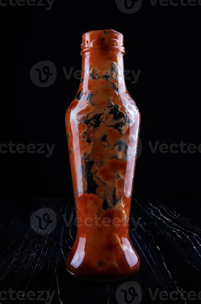 Tomate Soße . leeren Ketchup Flasche. Glas Flasche mit verbleibend Ketchup Innerhalb auf ein schwarz Hintergrund. foto