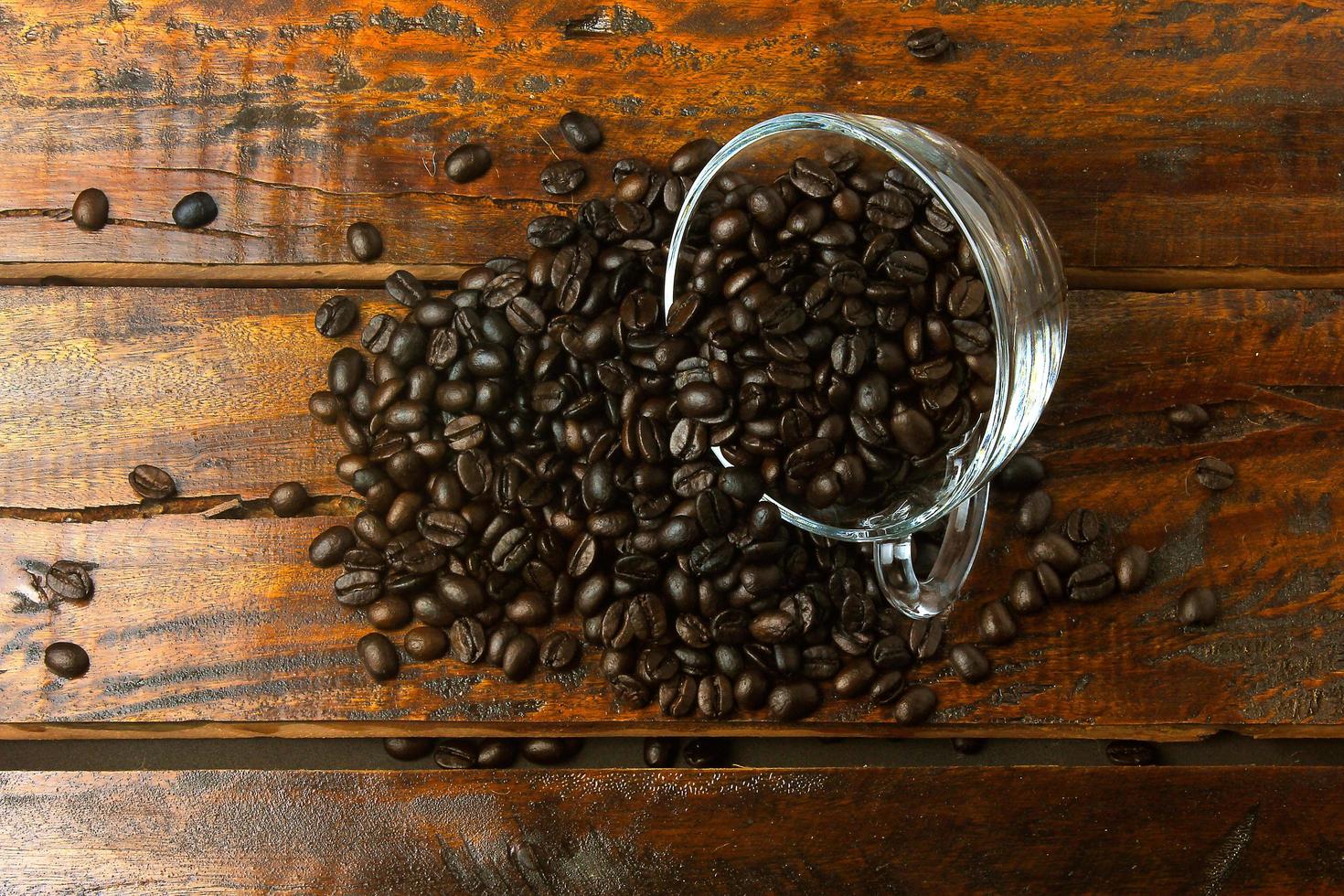 Glastasse mit gerösteten und frischen Kaffeebohnen über rustikalen Holztisch gegossen foto