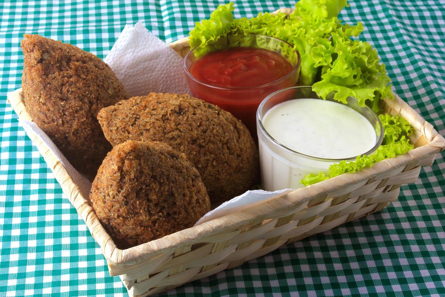 gebratener Kibbeh mit Tomatensauce im Korb, über rustikalem Holztisch foto