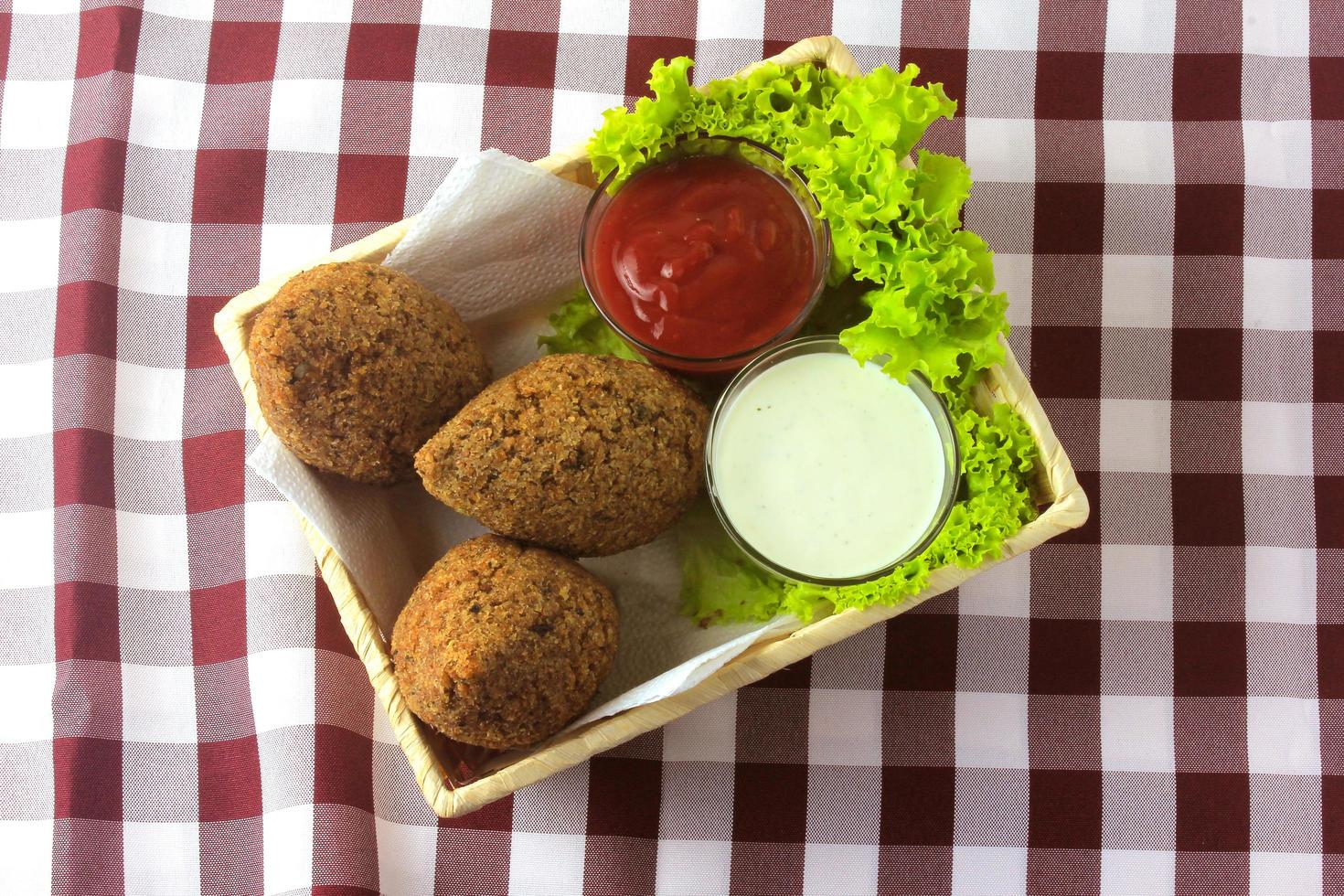 gebratener Kibbeh mit Tomatensauce im Korb, über rustikalem Holztisch foto