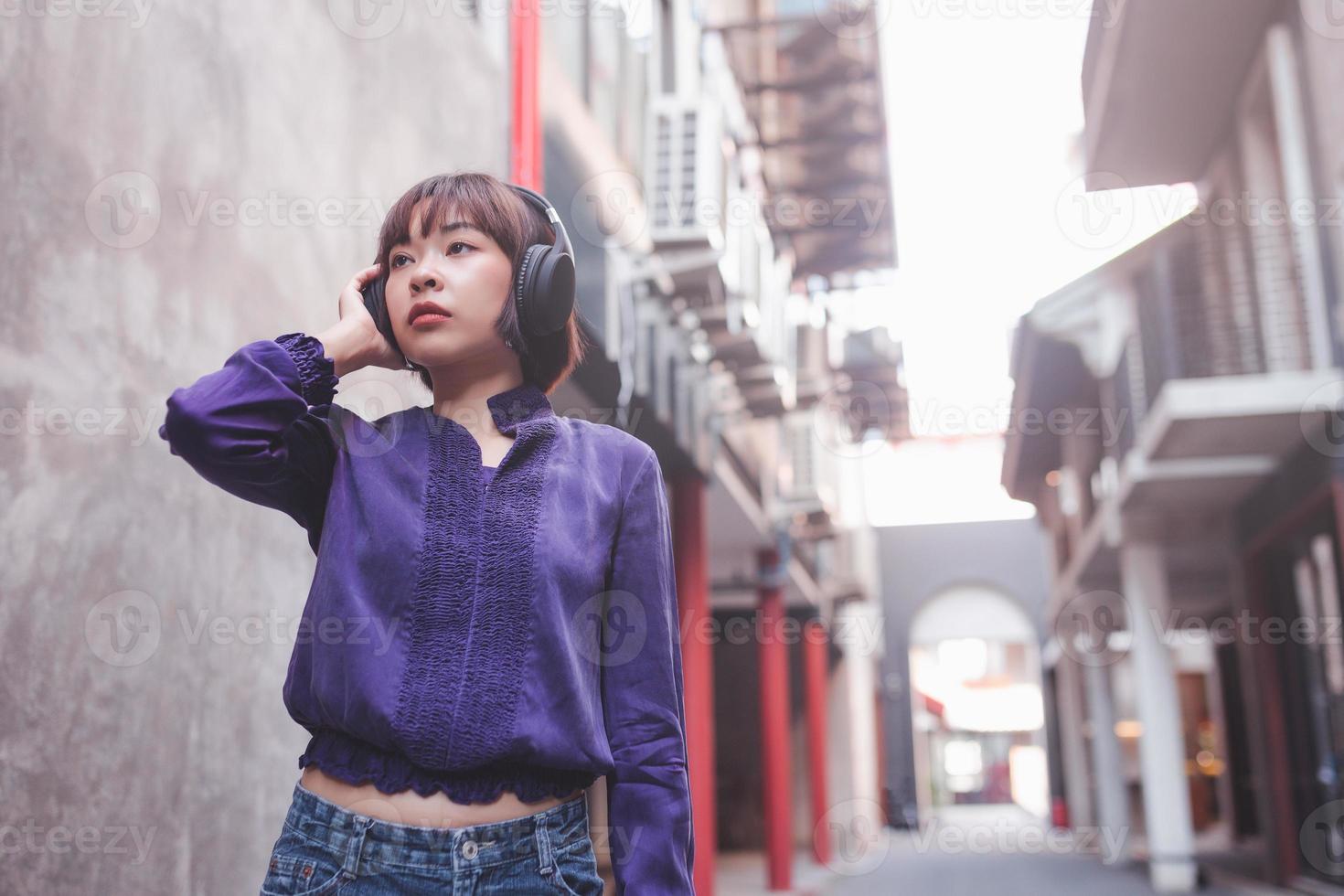 glückliche junge asiatische frau, die musik mit kopfhörern auf der straße hört foto