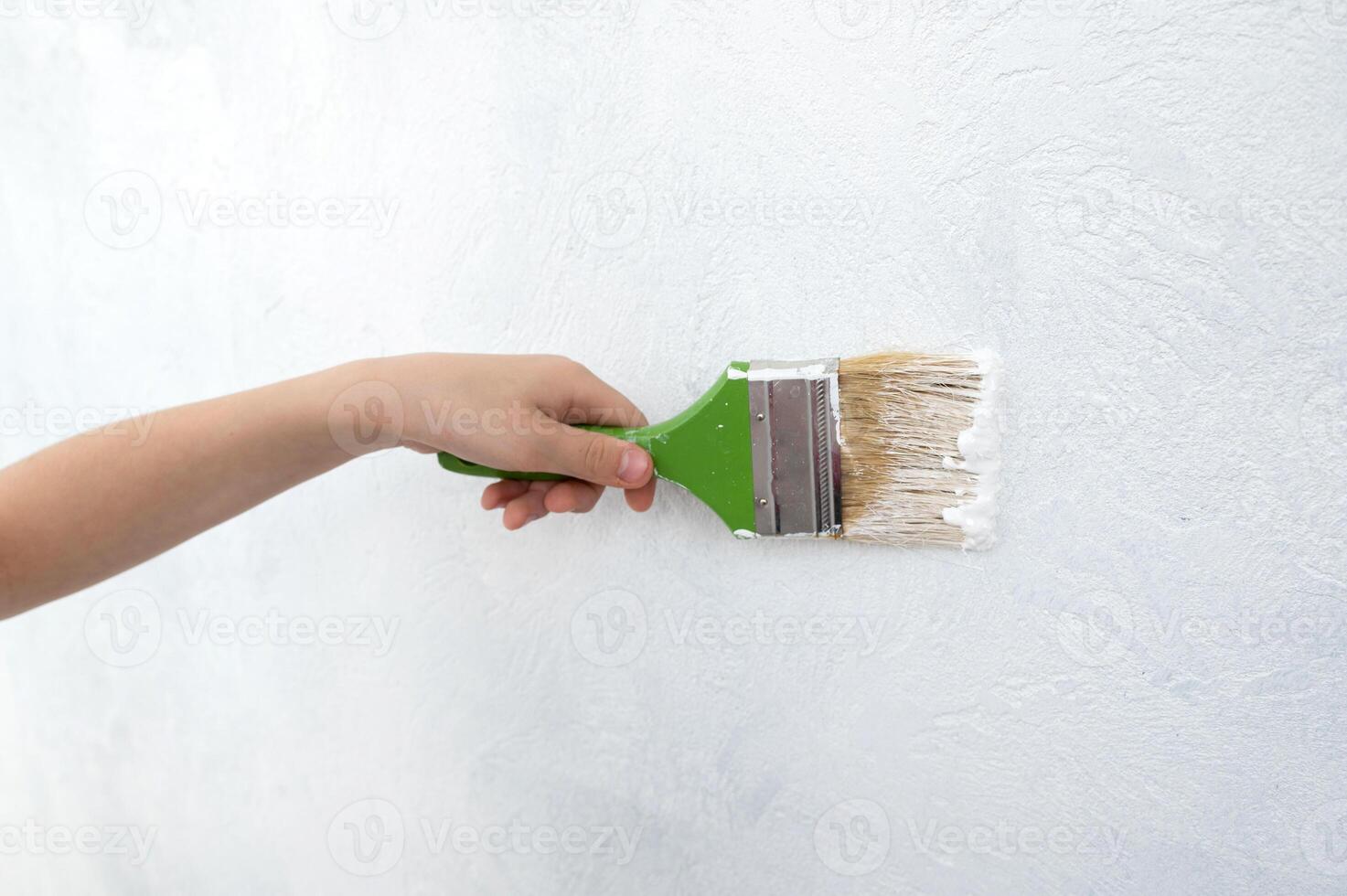 das Kinder Hand hält ein Farbe Bürste mit Weiß malen. Farbe das Mauer mit ein Konstruktion Bürste. foto